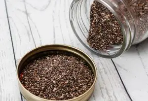 sementes de chia na tampa de um frasco de vidro aberto. o óleo de chia deriva dessas sementes