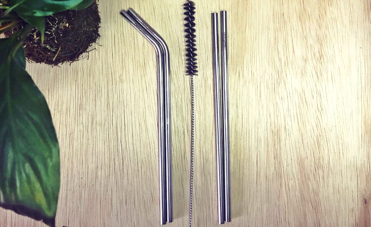 Fotografia colorida em ambiente interno de dois canudos curvados e dois canudos retos de inox com uma escova higienica entre os dois.
