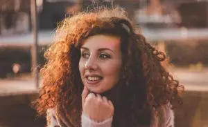 Mulher com mão no queixo e cabelo cacheados que usa shampoo Low Poo