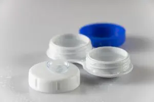 caixa de lente de contato destampada com uma lente em cima de uma das tampas