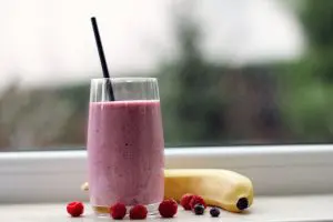 um smoothie roxo, ao lado de uma banana e algumas frutas vermelhas