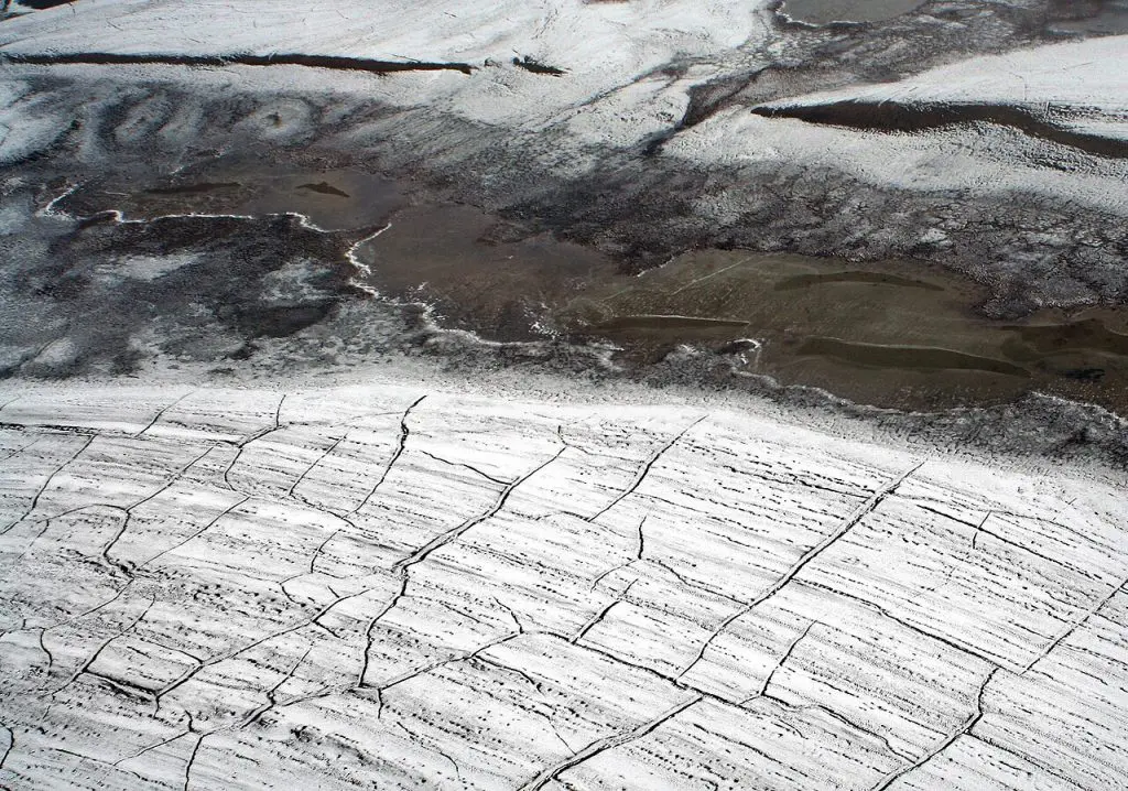 Imagem aérea mostrando rachaduras no permafrost no Alto Ártico, evidenciando os efeitos do degelo no solo permanentemente congelado.